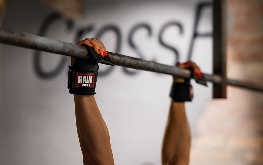 Lhikuva henkiln ksist roikkumassa tangossa, ksiss hnell RAW Supps LIfting Grips.